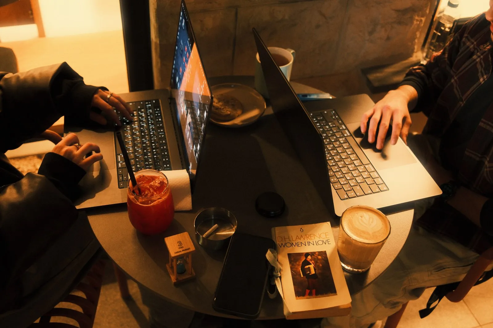 Two people at a cafe table late at night, booking from a laptop